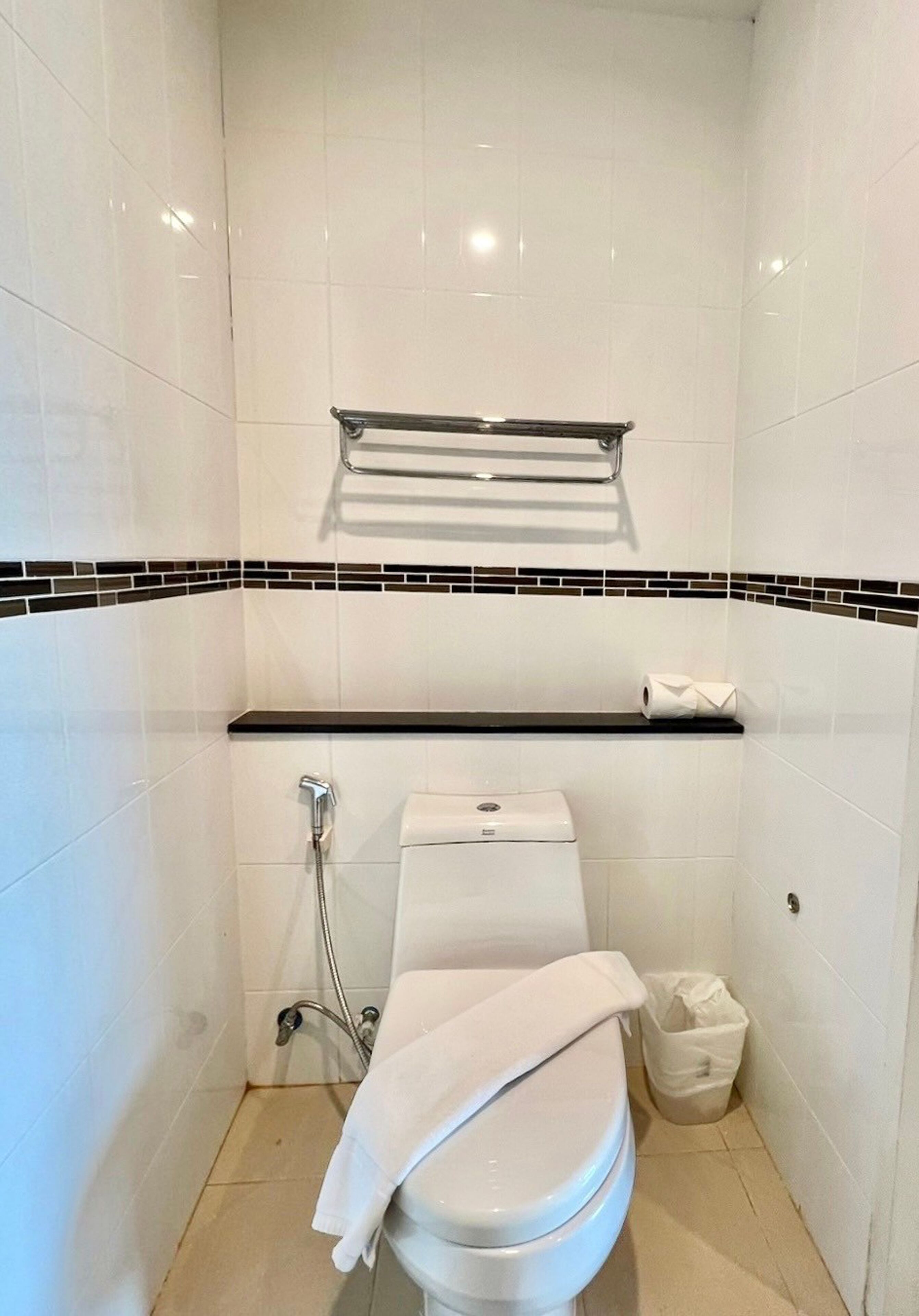 Un bagno moderno e piccolo, con piastrelle bianche, un WC, una doccia e un porta asciugamani.