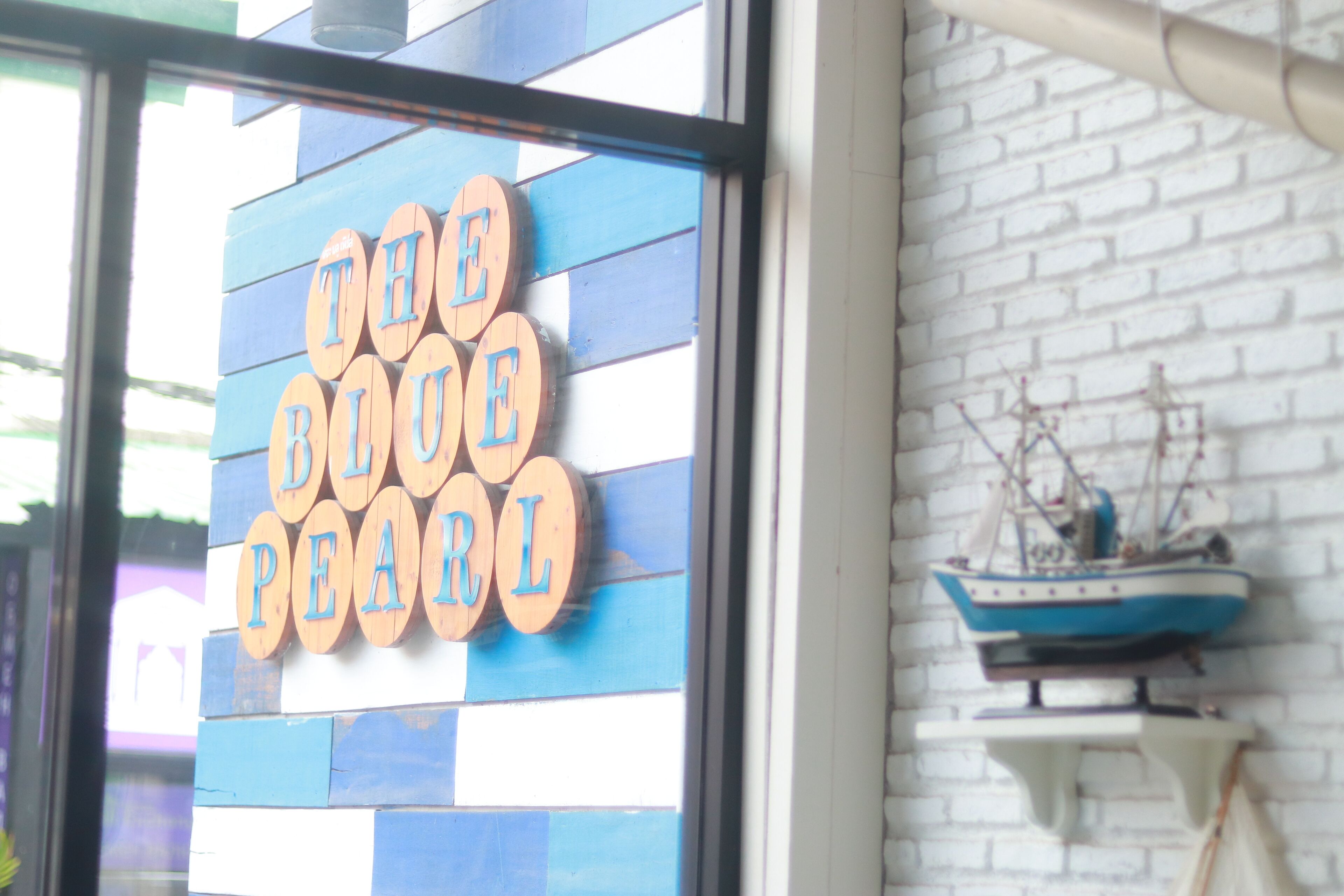 A sign with wooden letters spelling "THE BLUE PEARL" on a blue and white striped background.
