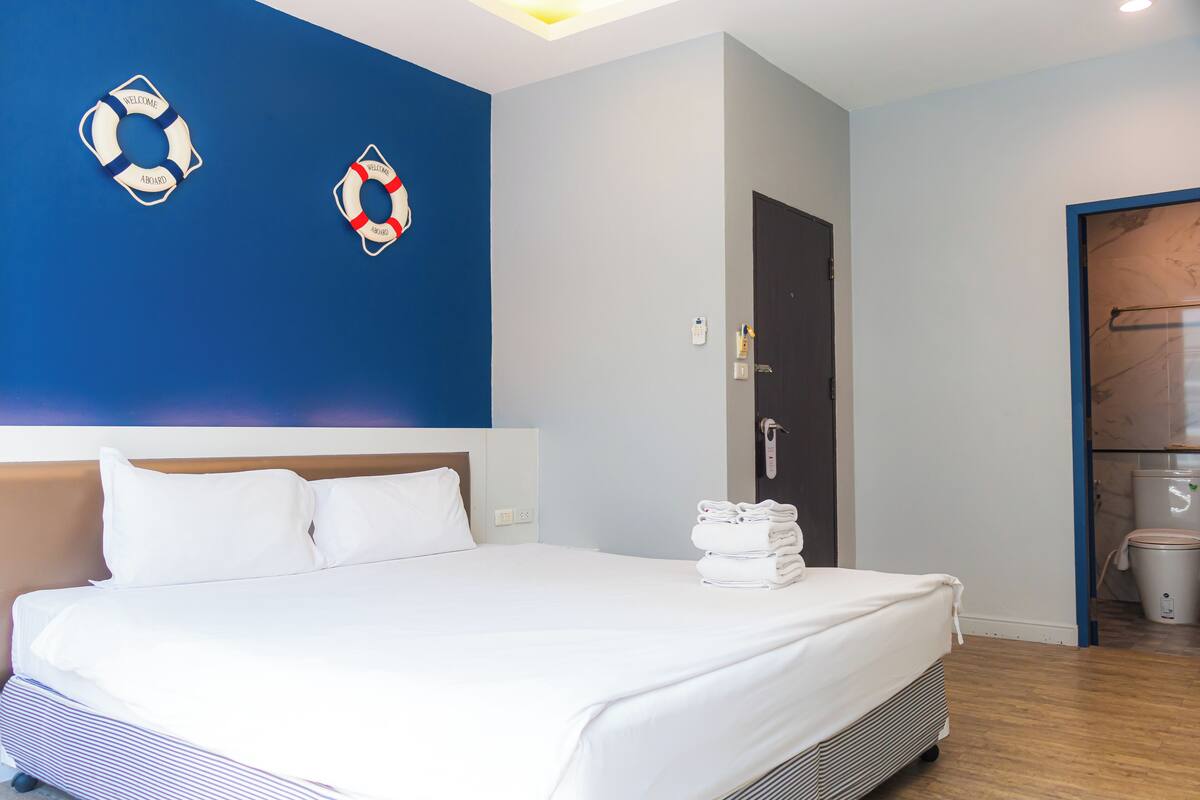 A hotel room with a large bed, a blue accent wall, and a door leading to a bathroom.