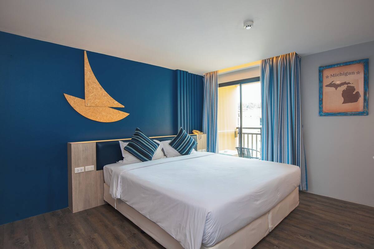 A hotel room with a large bed, a wooden headboard, a wall-mounted crescent moon decoration, a framed map of Michigan, and a balcony with curtains.