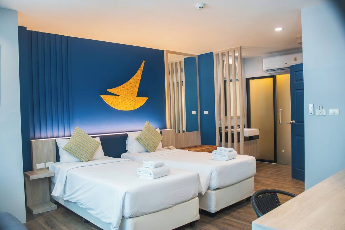 A hotel room with two beds, a large wall decoration, a desk, and a bathroom visible through a door.
