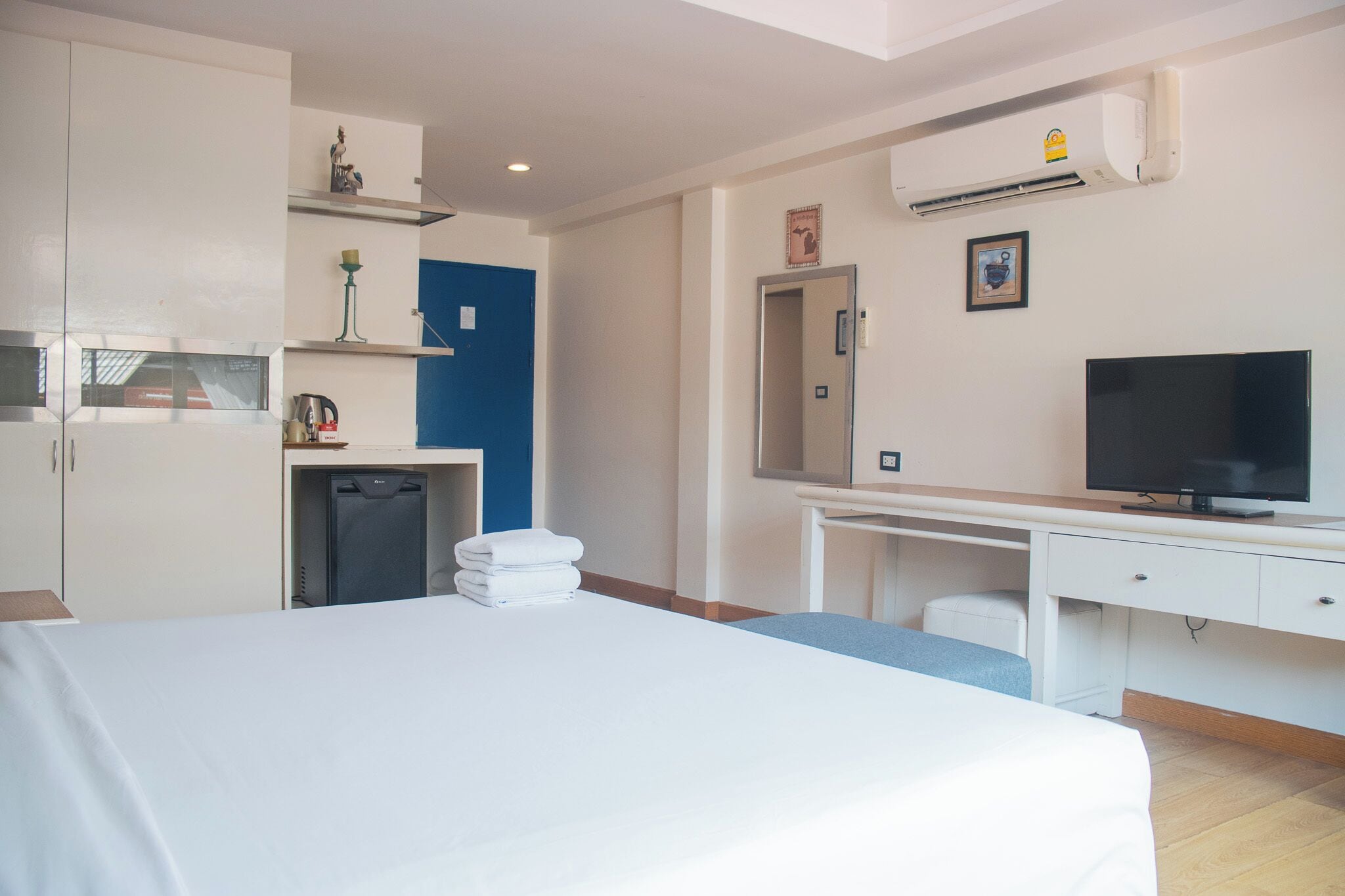 A hotel room with a bed, a desk with a television, a wardrobe, and a small kitchenette with a refrigerator.