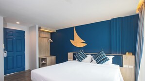 Habitación de hotel con una cama grande, un armario de madera, un escritorio con teléfono y una pared azul con un diseño de velero.