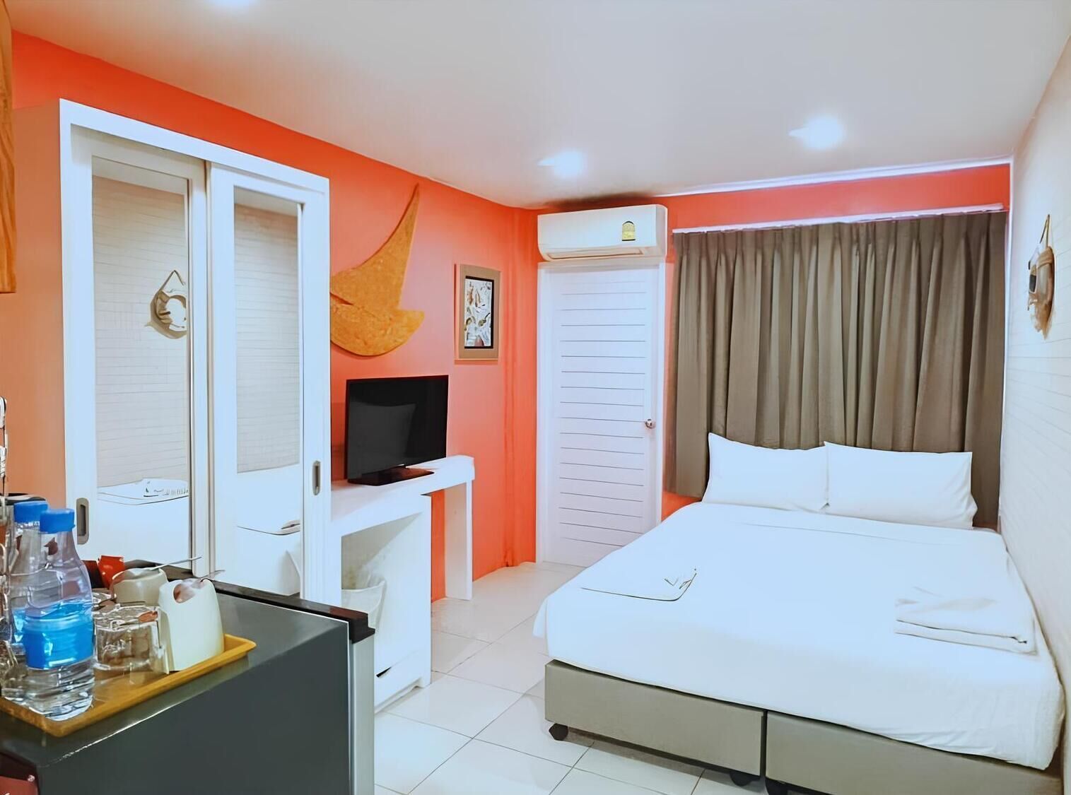 Una habitación de hotel con cama, escritorio con televisor, armario y aire acondicionado.
