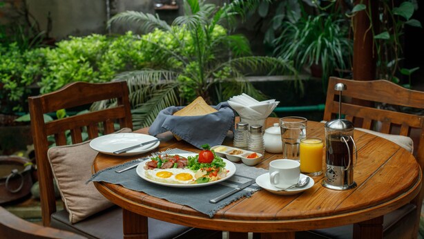 Una mesa redonda de madera con alimentos para el desayuno, como huevos, tomates y una cafetera.