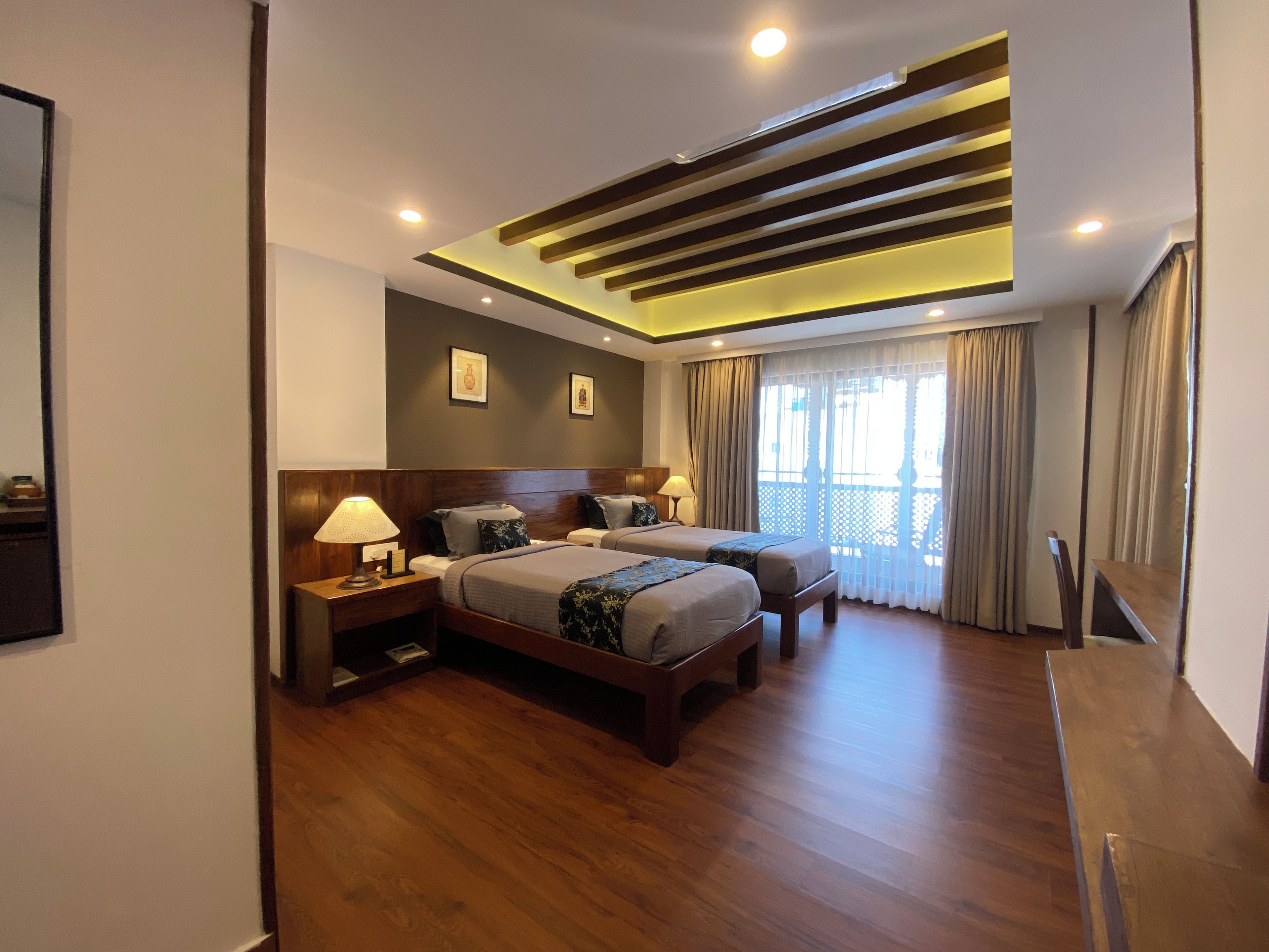 A modern hotel room with a large bed, bedside tables, a desk, and a ceiling with exposed beams.