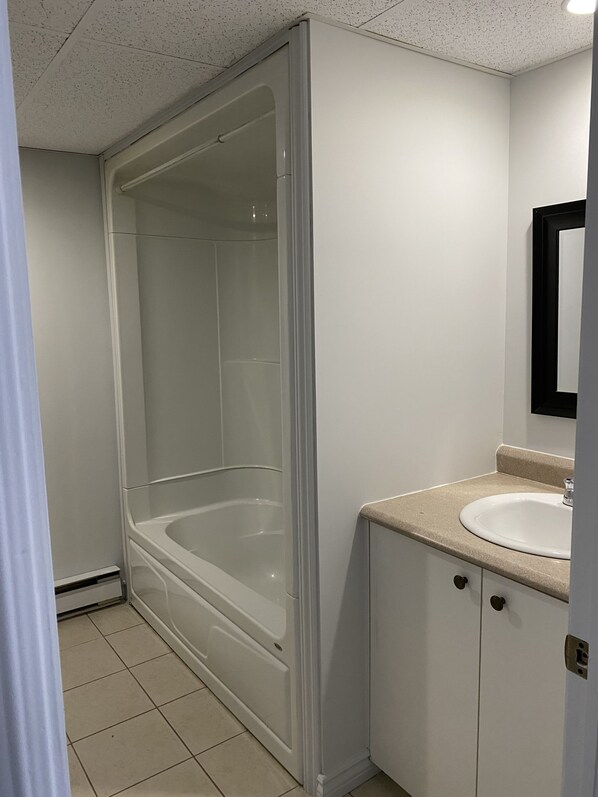 A bathroom with a glass-enclosed shower, a sink with a countertop, and a mirror on the wall.