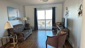 Una sala de estar con sofá, una silla, una lámpara, un televisor y un balcón con vistas.