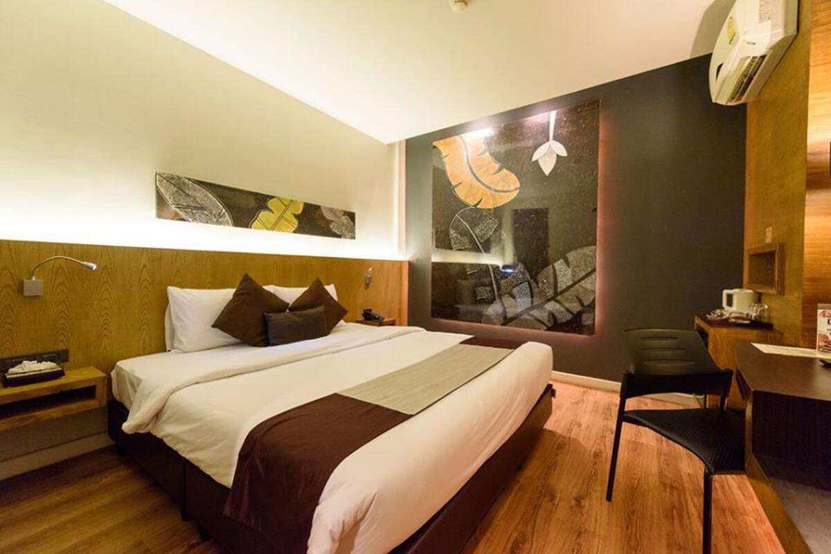 Quarto de hotel com uma cama grande, uma escrivaninha e uma cadeira. Há uma janela com vista para um edifício.
