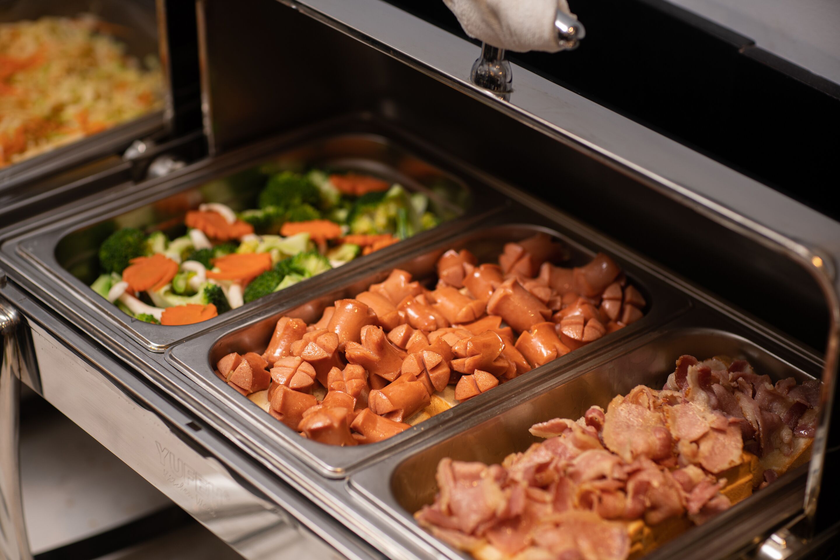 Ein Buffet mit verschiedenen Speisen, darunter Gemüse, Hot Dogs und Speck.