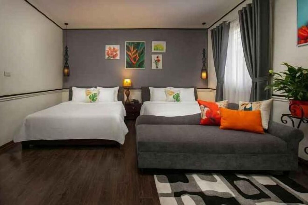 A hotel room with two beds, a sofa, a rug, and artwork on the wall.