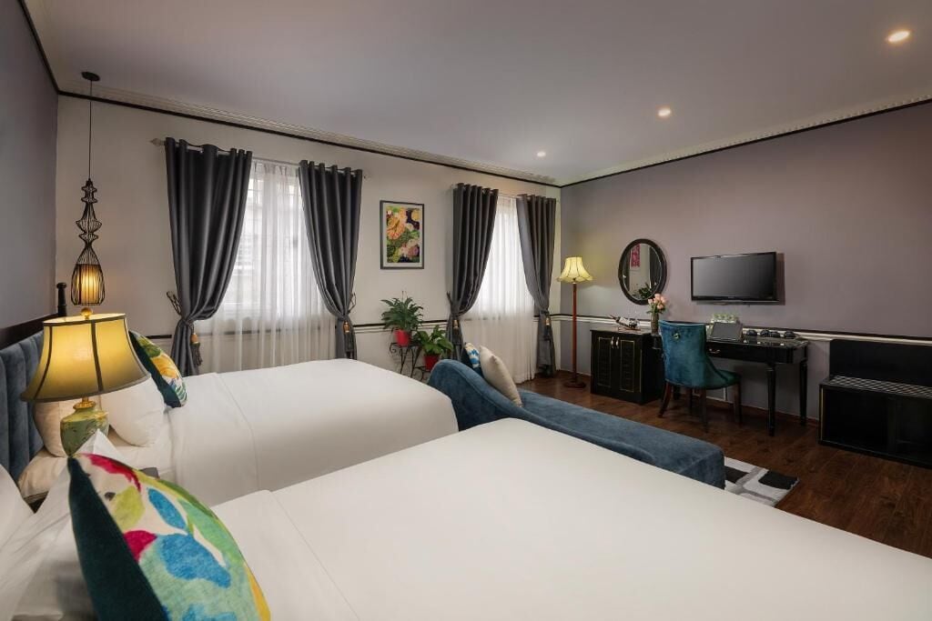 A hotel room with two beds, a desk, a chair, a TV, and curtains.