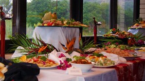 Taula de buffet amb diversos plats, incloent amanides, carns i pans, davant un finestral que mostra vistes a vegetació.