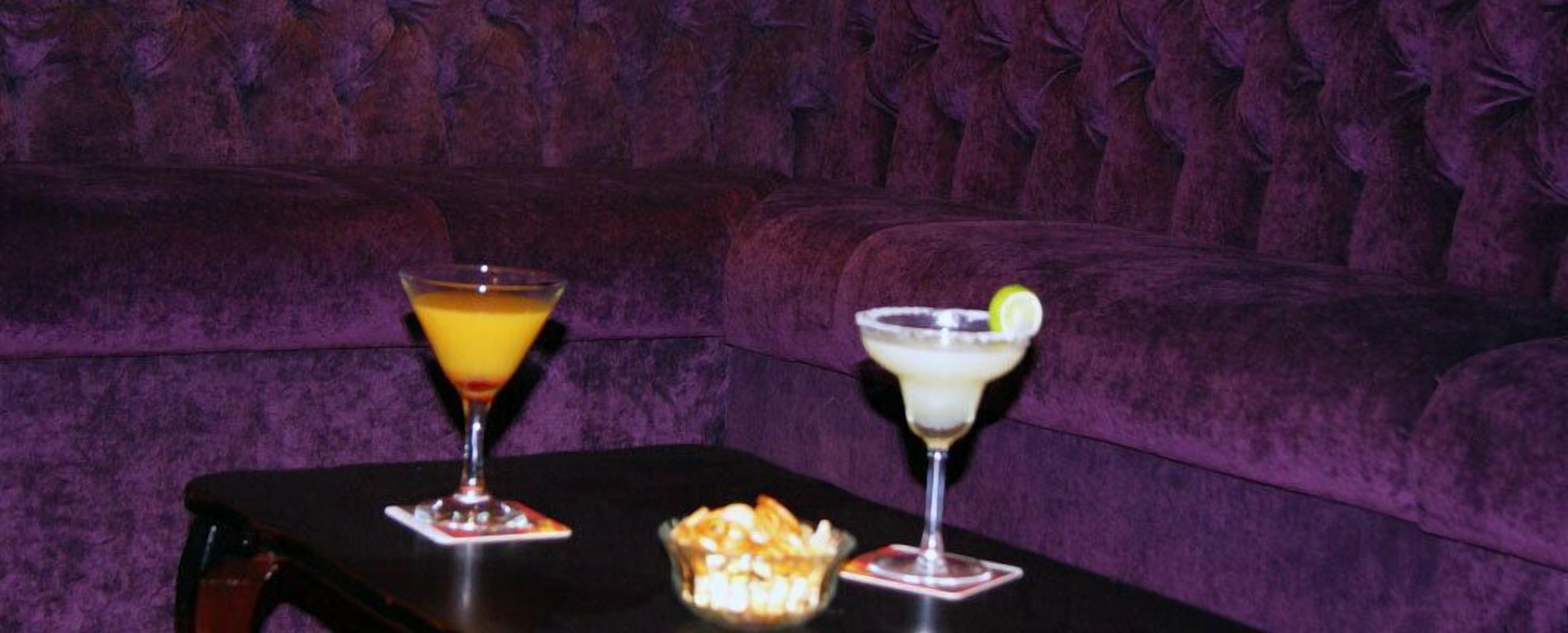 A table with two drinks and a bowl of snacks on a black tablecloth.