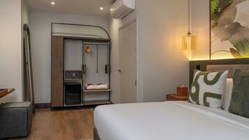 A hotel room with a bed, a wardrobe, a small table, and a wall-mounted air conditioner.