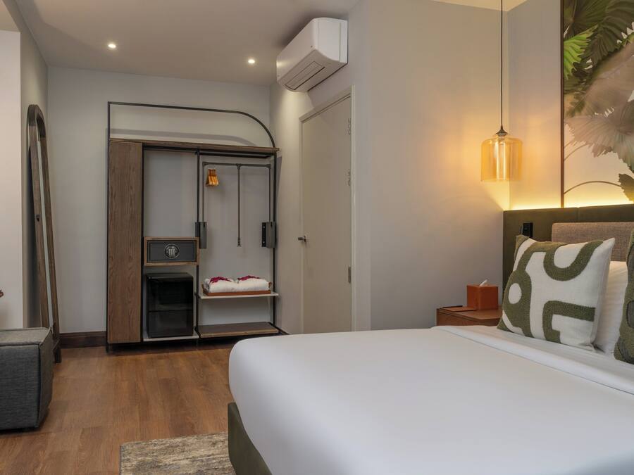 A hotel room with a bed, a wardrobe, a small table, and a wall-mounted air conditioner.