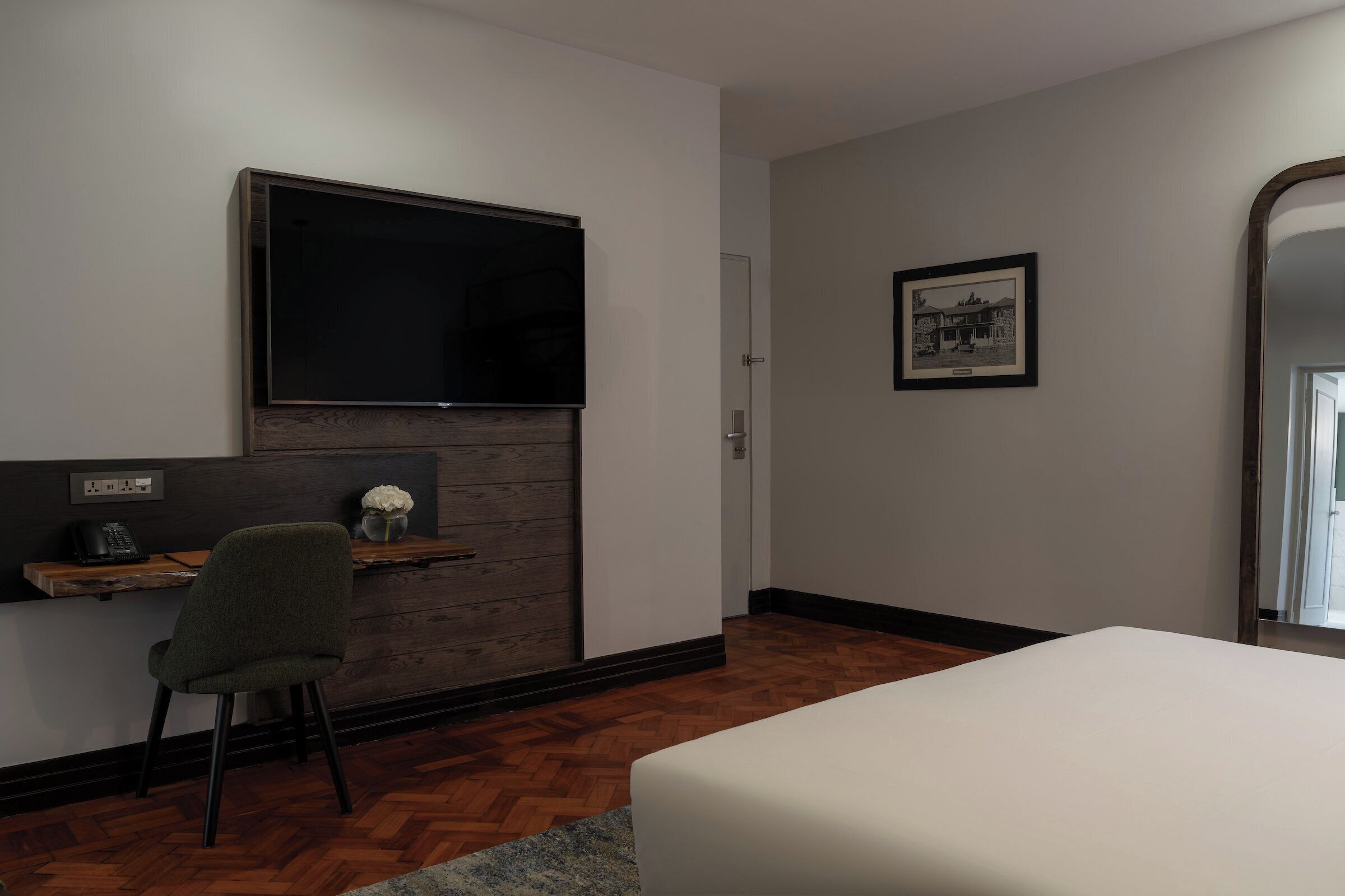 Quarto de hotel moderno com uma cama grande, uma escrivaninha com cadeira, uma TV de tela plana fixada em um painel de madeira e um quadro na parede.