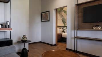 Una sala de estar moderna con un sofá gris, una mesa de centro redonda de madera, una mesita auxiliar negra con un florero, un cuadro en la pared, un televisor de pantalla plana montado en una pared de madera y un estante con objetos decorativos.