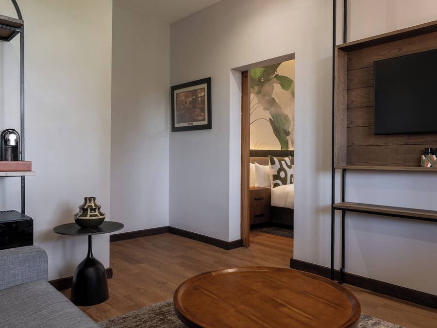 Una sala de estar moderna con un sofá gris, una mesa de centro redonda de madera, una mesita auxiliar negra con un florero, un cuadro en la pared, un televisor de pantalla plana montado en una pared de madera y un estante con objetos decorativos.