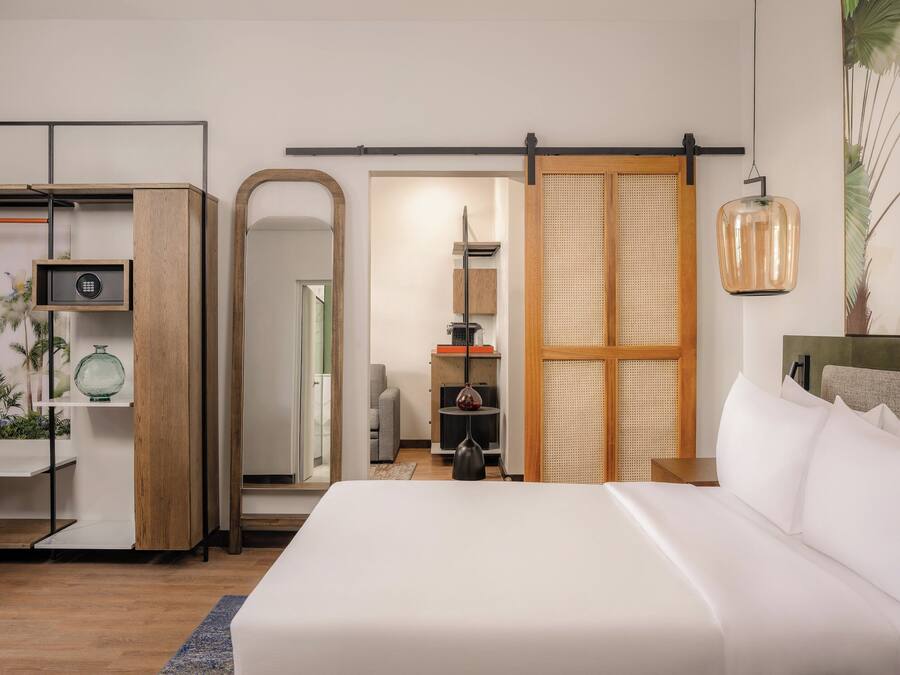 A modern bedroom with a large bed, a wooden wardrobe, a mirror, and a hanging light fixture.