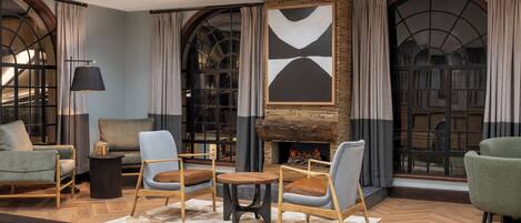 A cozy lounge area with a fireplace, comfortable seating, and large windows with curtains.