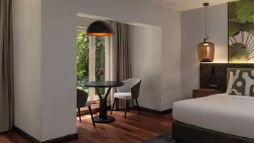 A hotel room with a bed, a round table with two chairs, a large window with curtains, and a hanging pendant light.