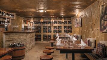 A cozy bar area with wooden shelves, a stone wall, and a seating area with benches and tables.