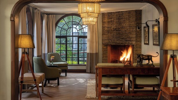 A cozy room with a fireplace, wooden furniture, and a large window with curtains. - Fairview Hotel Nairobi, Vignette Collection by IHG (Nairobi)