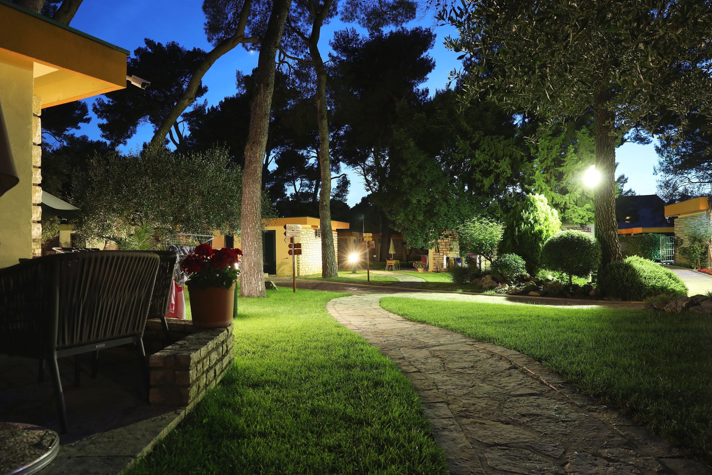 A well-lit outdoor area with a stone pathway, a seating area with a table and chairs, and a potted plant.