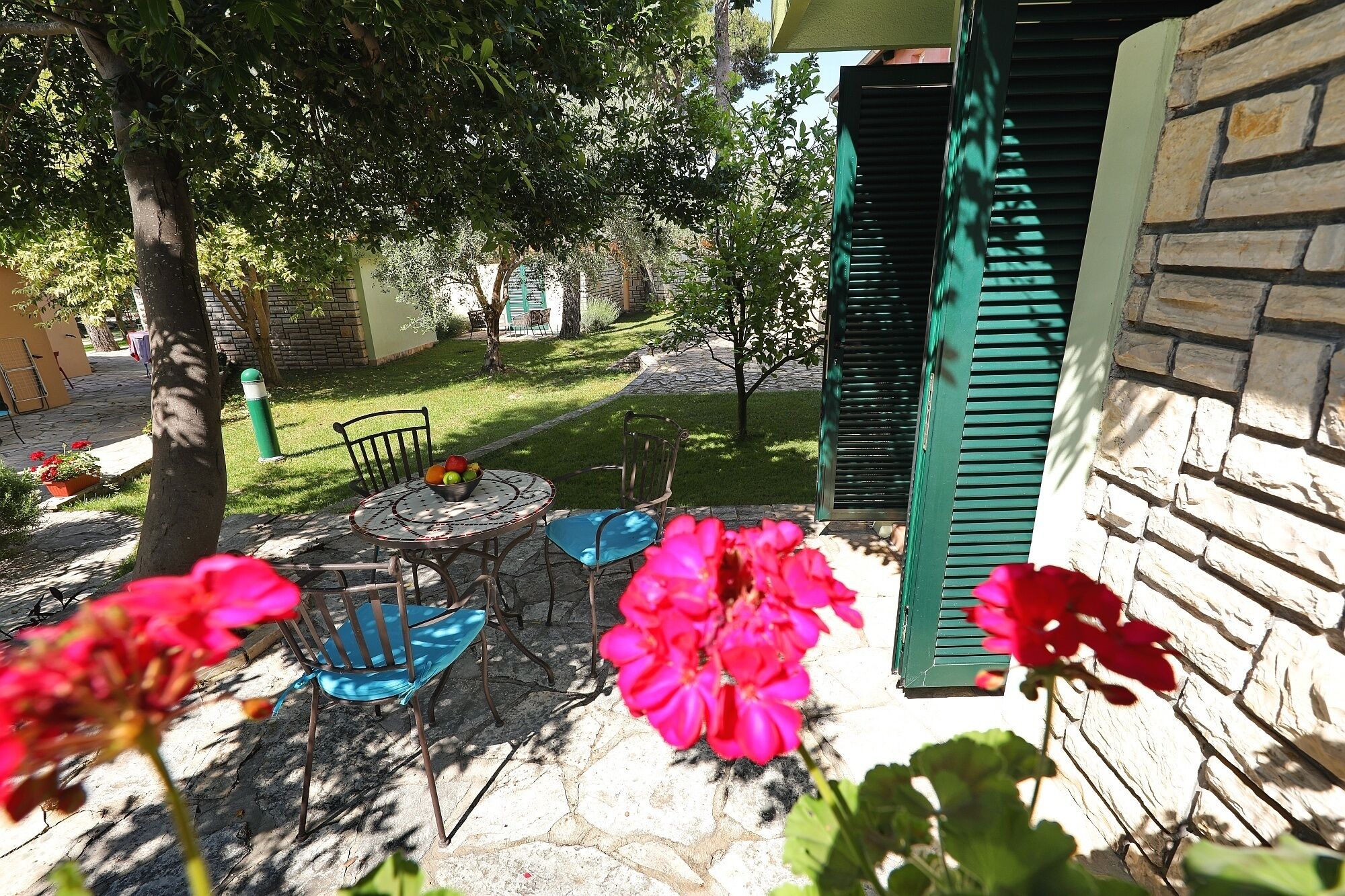 A patio with a stone table, two chairs, and a bowl of fruit.