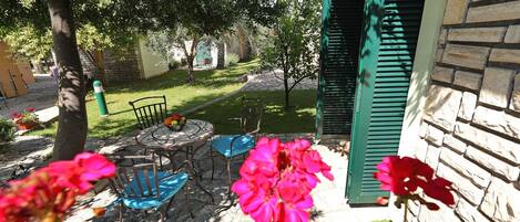 A patio with a stone table, two chairs, and a bowl of fruit.