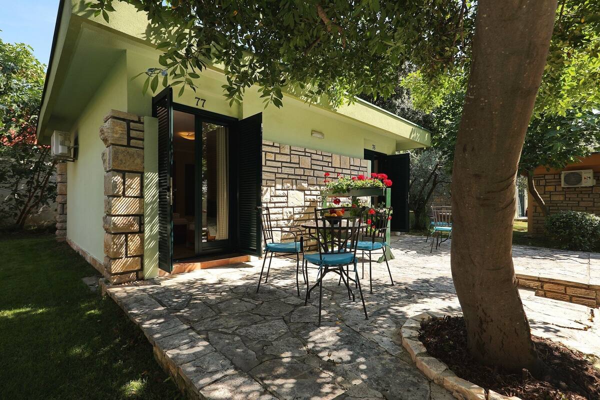 Une terrasse avec un sol en pierre, une table entourée de chaises et un petit jardin agrémenté d’un arbre et de fleurs.