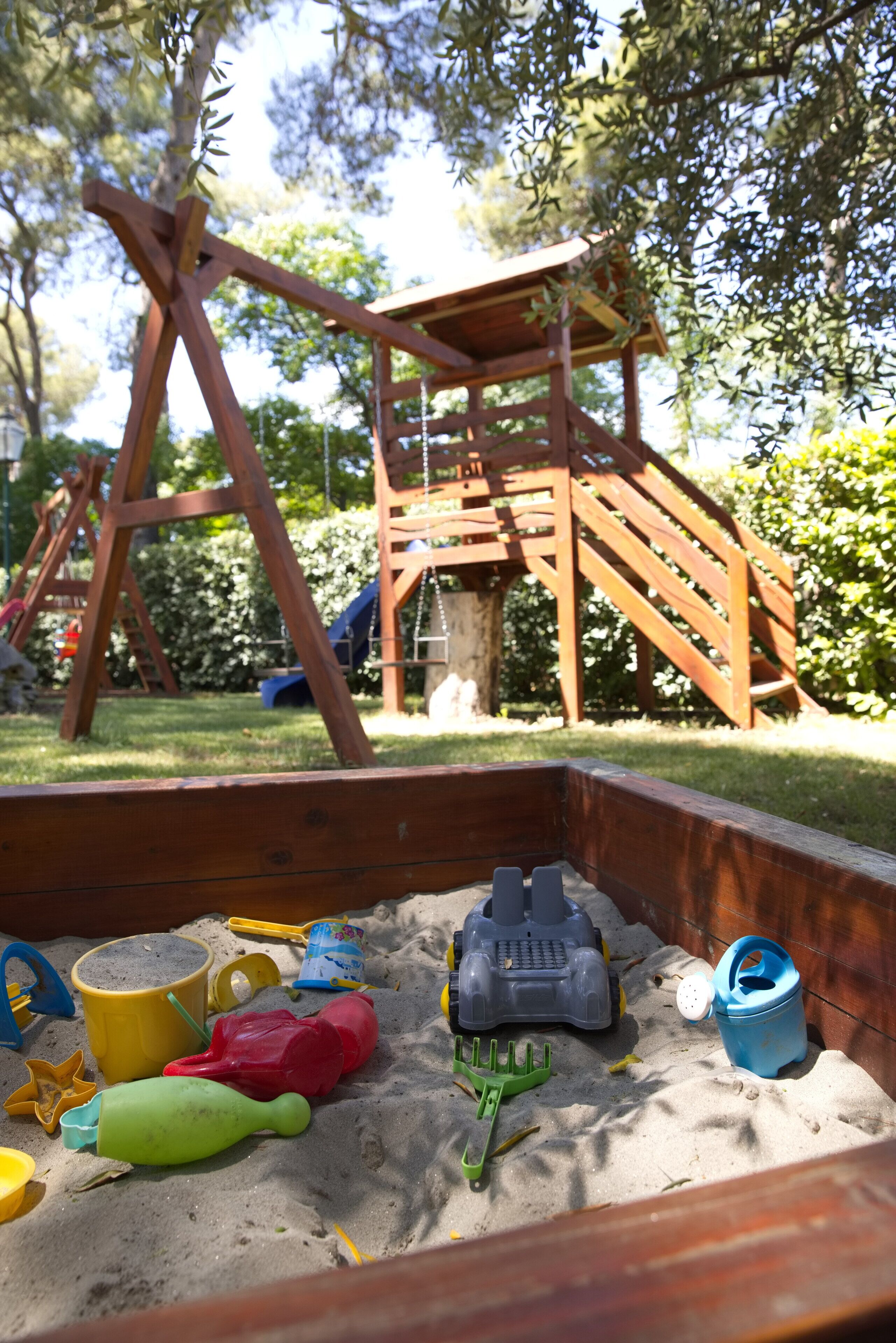 A wooden swing set and a sandbox with toys.