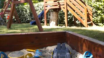 A wooden swing set and a sandbox with toys.