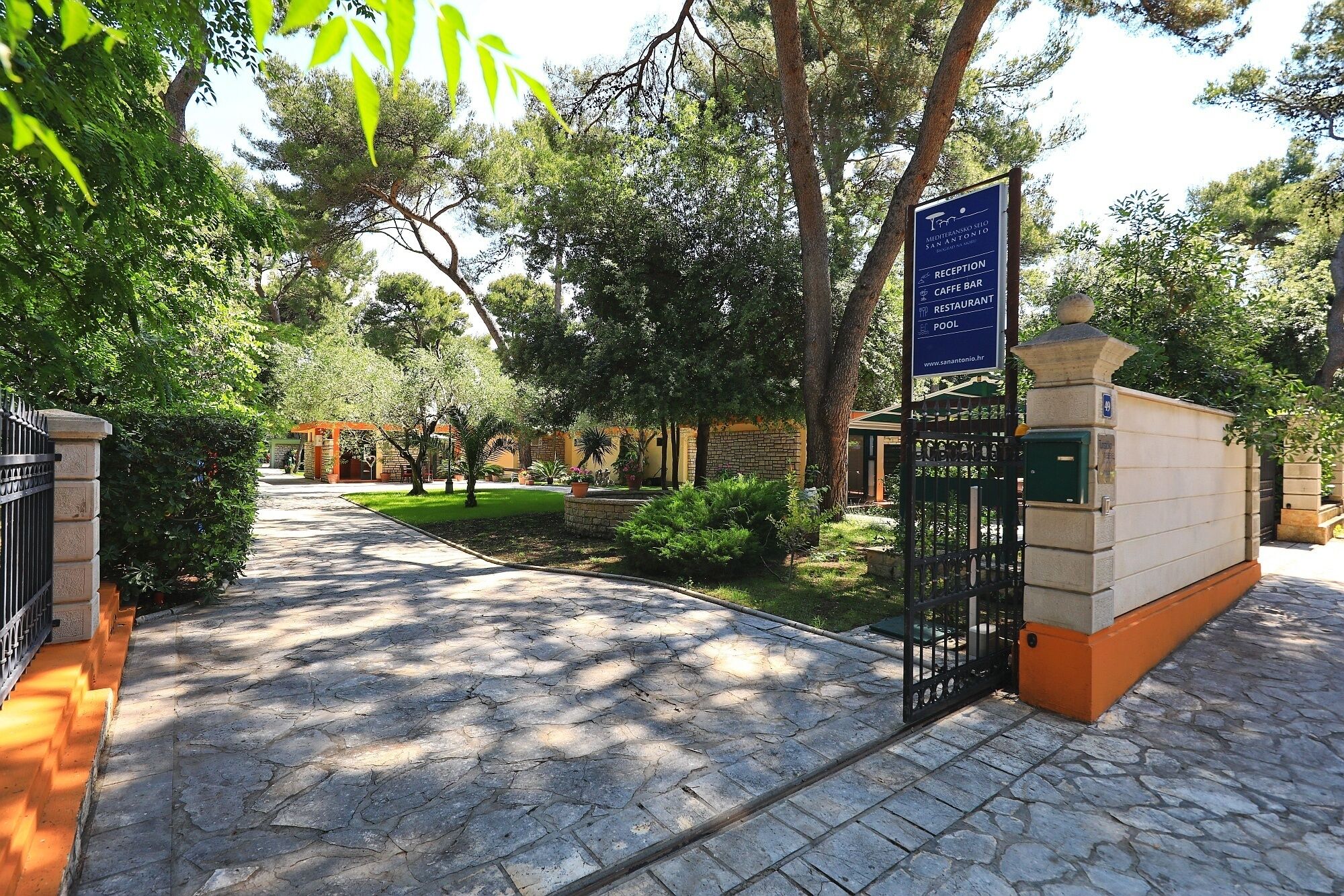 A stone pathway leading to a reception area with a sign indicating amenities like a reception, cafe bar, restaurant, and pool.