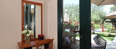 Una habitación con un escritorio de madera, una silla, un espejo y vistas a un patio exterior con una mesa y sillas.