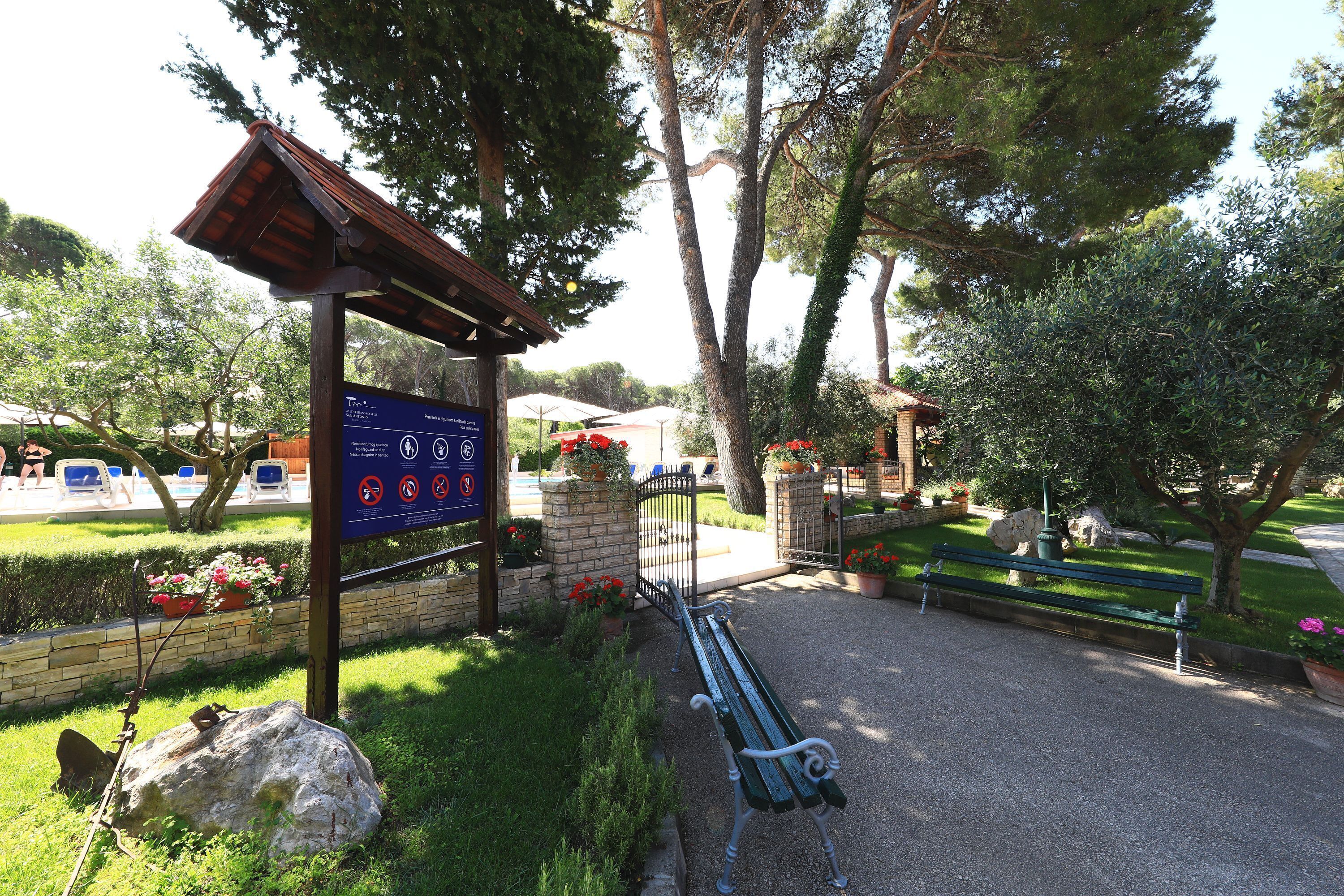 A park entrance with a sign, a bench, and a pathway.