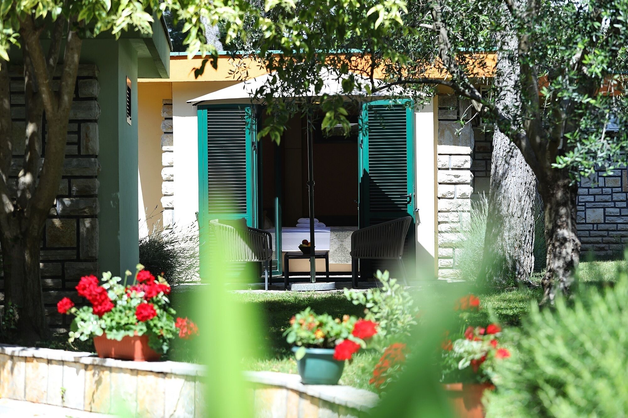 Une pièce comprenant un lit, une chaise et une table, avec vue sur un jardin et un bâtiment en arrière-plan.
