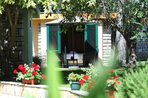 Une pièce comprenant un lit, une chaise et une table, avec vue sur un jardin et un bâtiment en arrière-plan.
