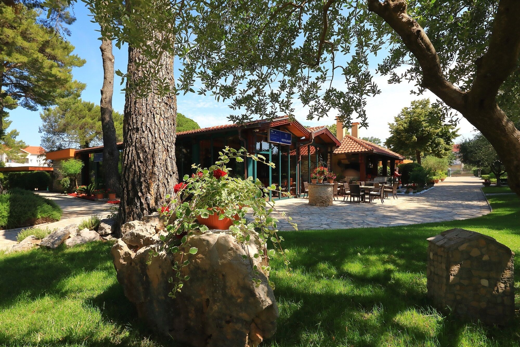 A restaurant with outdoor seating, surrounded by greenery and stone structures.
