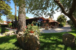 Un restaurant doté d’une terrasse, entouré de verdure et de constructions en pierre.