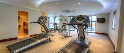 Une salle de sport équipée de tapis de course, de vélos d’exercice et d’un téléviseur fixé au mur.