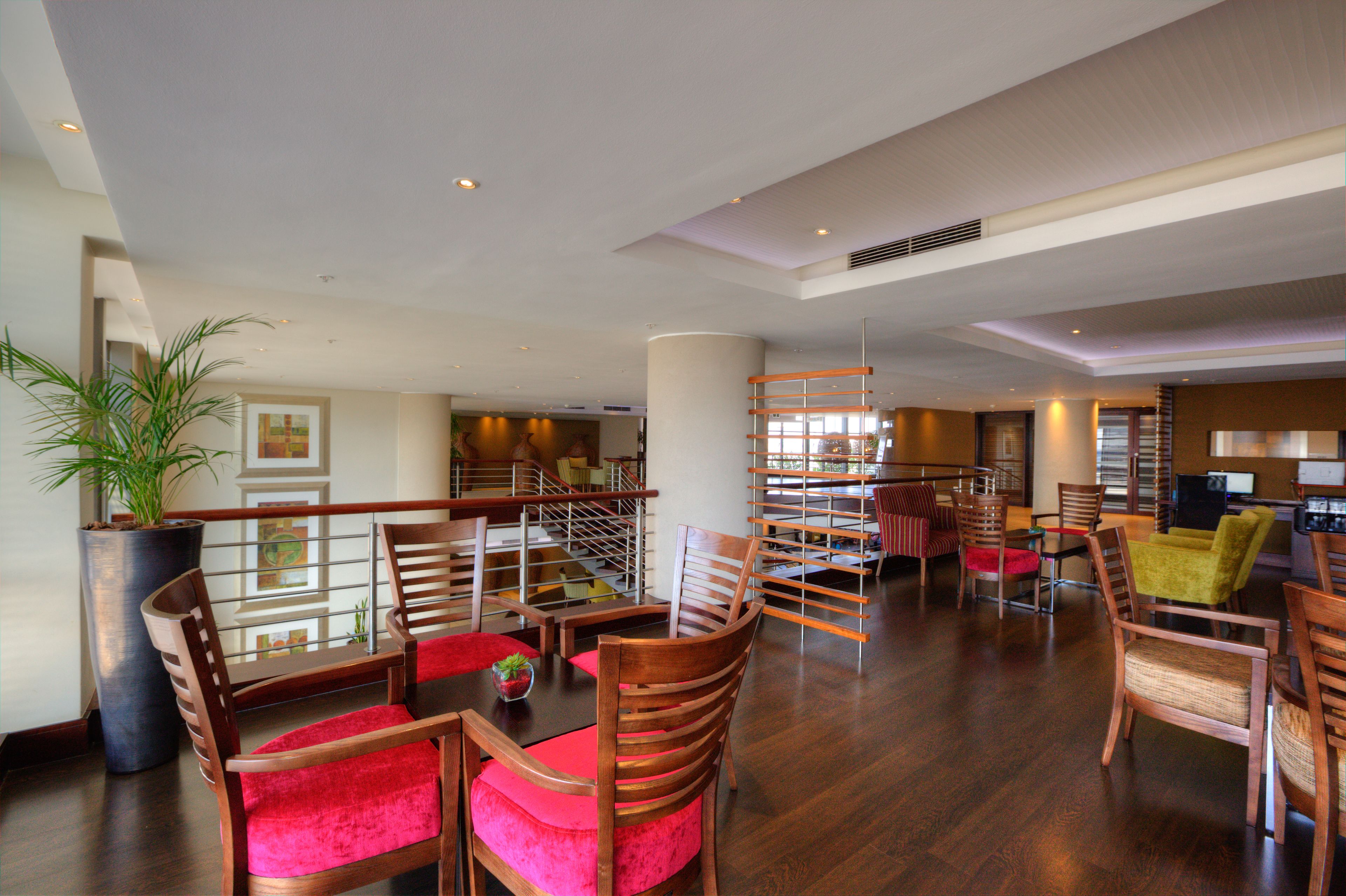 A spacious hotel lobby with wooden furniture, a large potted plant, and a view of the dining area.