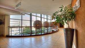 Un'ampia hall con grandi finestre, una pianta in vaso e una ringhiera moderna.