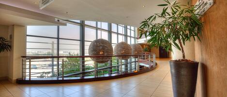 Un hall amplio con ventanas grandes, una planta en maceta y una barandilla moderna.