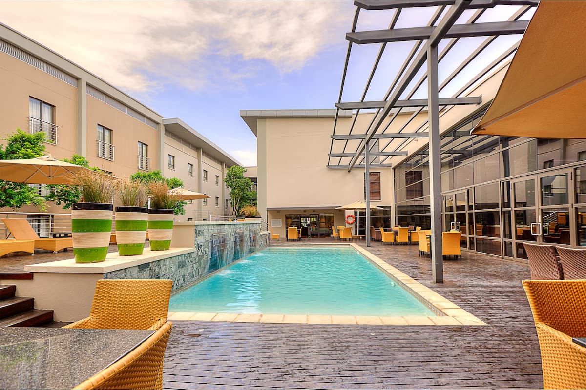 A swimming pool with lounge chairs and umbrellas, surrounded by buildings with large windows and a covered patio area.