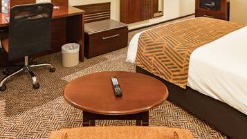 Een hotelkamer met een bed, een bureau, een stoel, een tafeltje en een prullenbak.