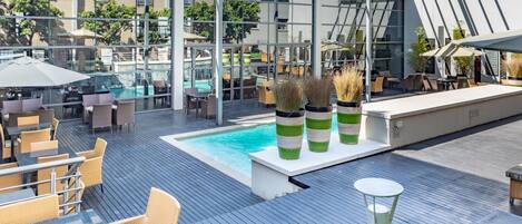 A rooftop pool area with outdoor seating and a glass-enclosed lounge.