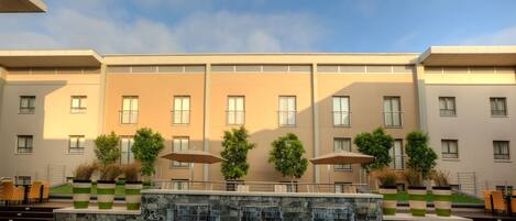 A hotel pool area with a waterfall feature, outdoor seating, and a view of the building facade.