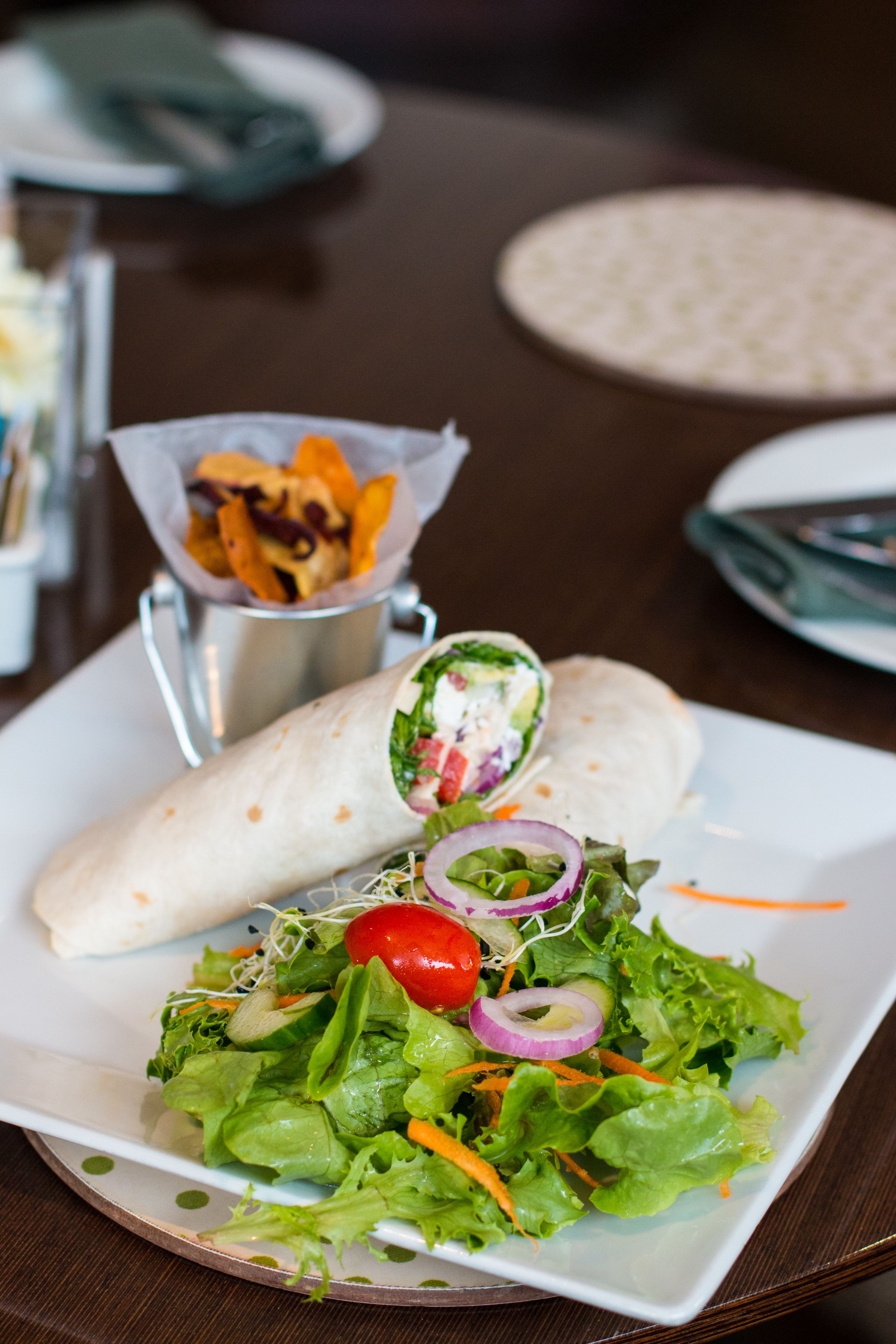 A plate with a wrap and a salad, and a small container of fries.